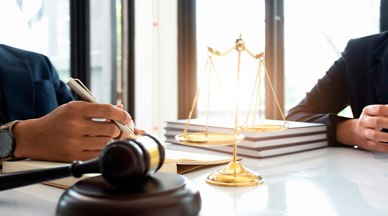 Dois advogados de terno em reunião com martelo de juiz e balança da justiça dourada sobre livros em mesa branca representando anulação de usucapião