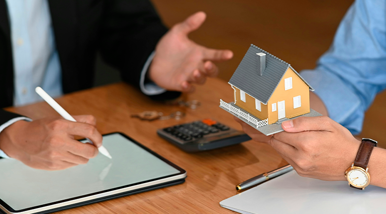 Cliente segurando maquete de casa amarela durante reunião com advogado que assina tablet em escritório com calculadora sobre mesa, representando consultoria de advogado especializado em sucessão em Curitiba para inventário e herança de imóvel